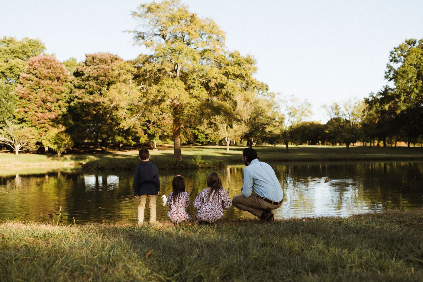 A father and three children watching ducks at the edge of a pond on an autumn afternoon