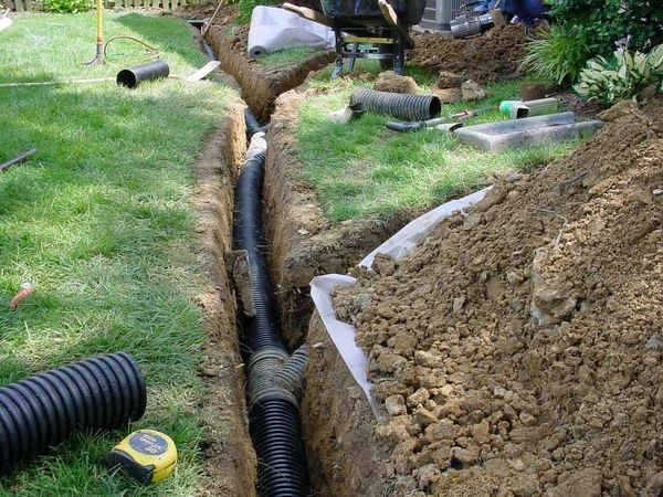Corrugated drain pipe being installed in an open trench beside a lawn