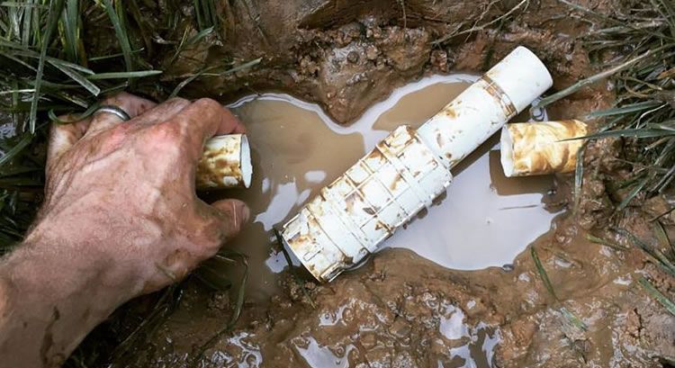 Hands repairing a broken irrigation pipe in a wet trench