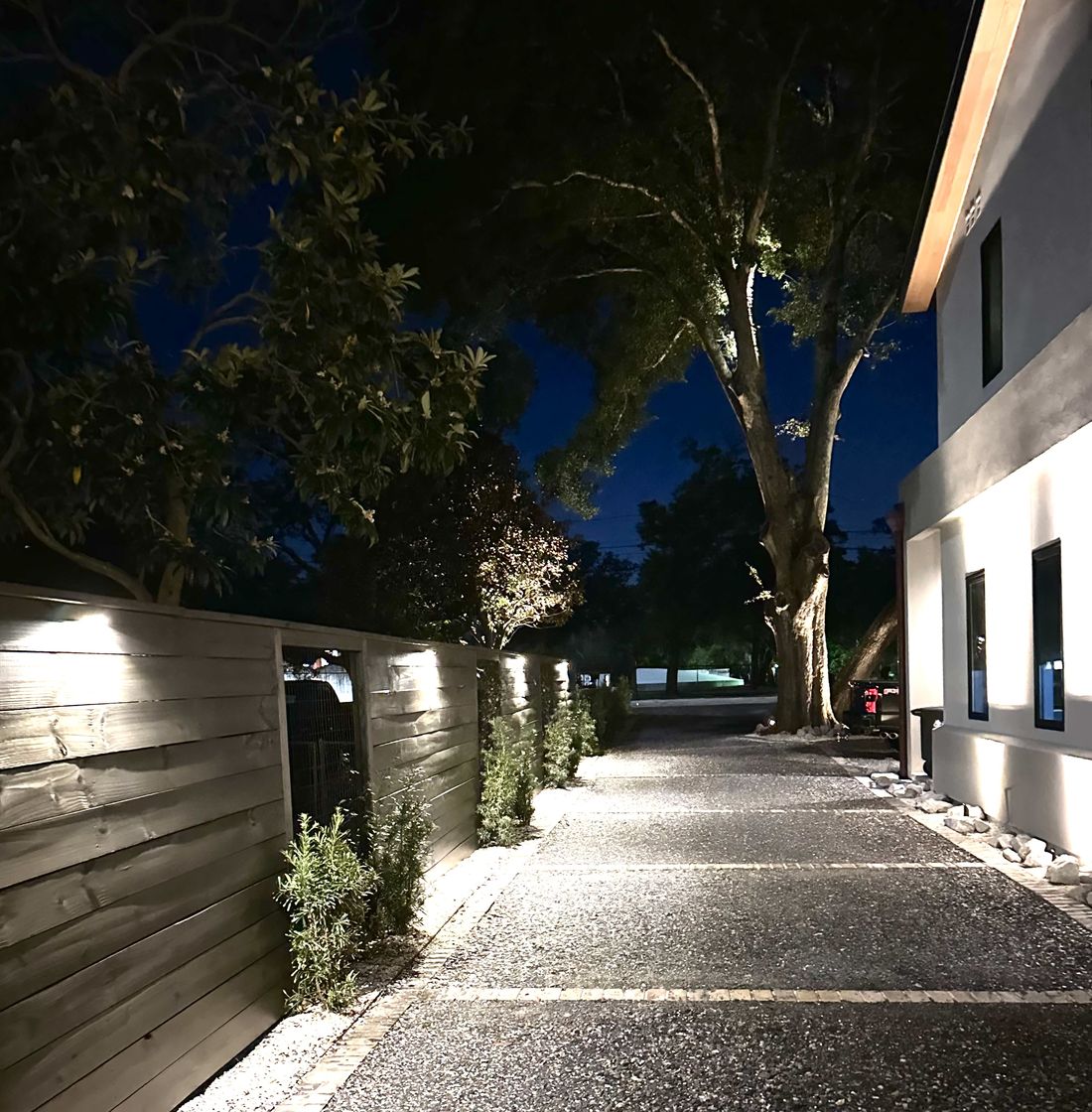 Landscape lighting illuminating a fence line, oaks, and driveway at night