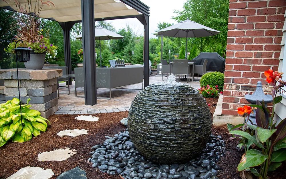 Stacked-slate sphere fountain in a mulched bed beside a paver patio